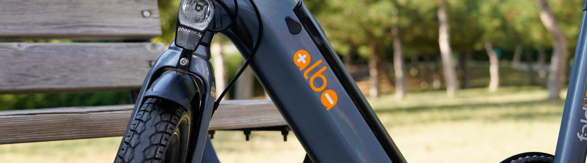 Alba Fold X Electric bike in dark grey colour resting against bench in park